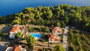 An aerial view of a coastal property with a swimming pool, terraced houses, and dense greenery. - Kamelia Villas in Alonissos (Alonissos)