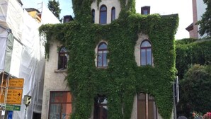 Ein mit Efeu bewachsenes Gebäude im traditionellen Baustil, mit zahlreichen Fenstern und einem zentralen Eingang.