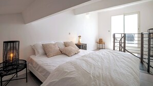 Un dormitorio con una cama grande, una silla, una mesita de noche y un balcón con barandilla.