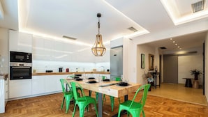 A modern kitchen with white cabinets, a built-in oven, and a dining area with a wooden table and green chairs. - MZ Kolonaki (Athina)
