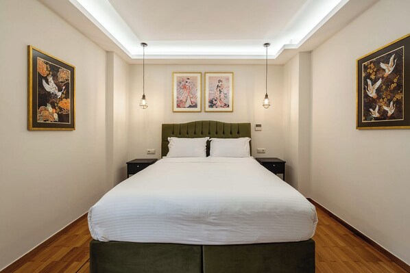Un dormitorio bien iluminado con una cama grande, dos mesitas de noche y cuadros en las paredes.