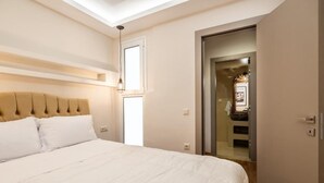 A bedroom with a large bed, a headboard, a window, and a door leading to a bathroom. - MZ Kolonaki (Athina)