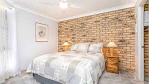 Une chambre avec un mur décoré d’un motif en briques, un lit recouvert d’une courtepointe, deux lampes de chevet et un ventilateur de plafond.