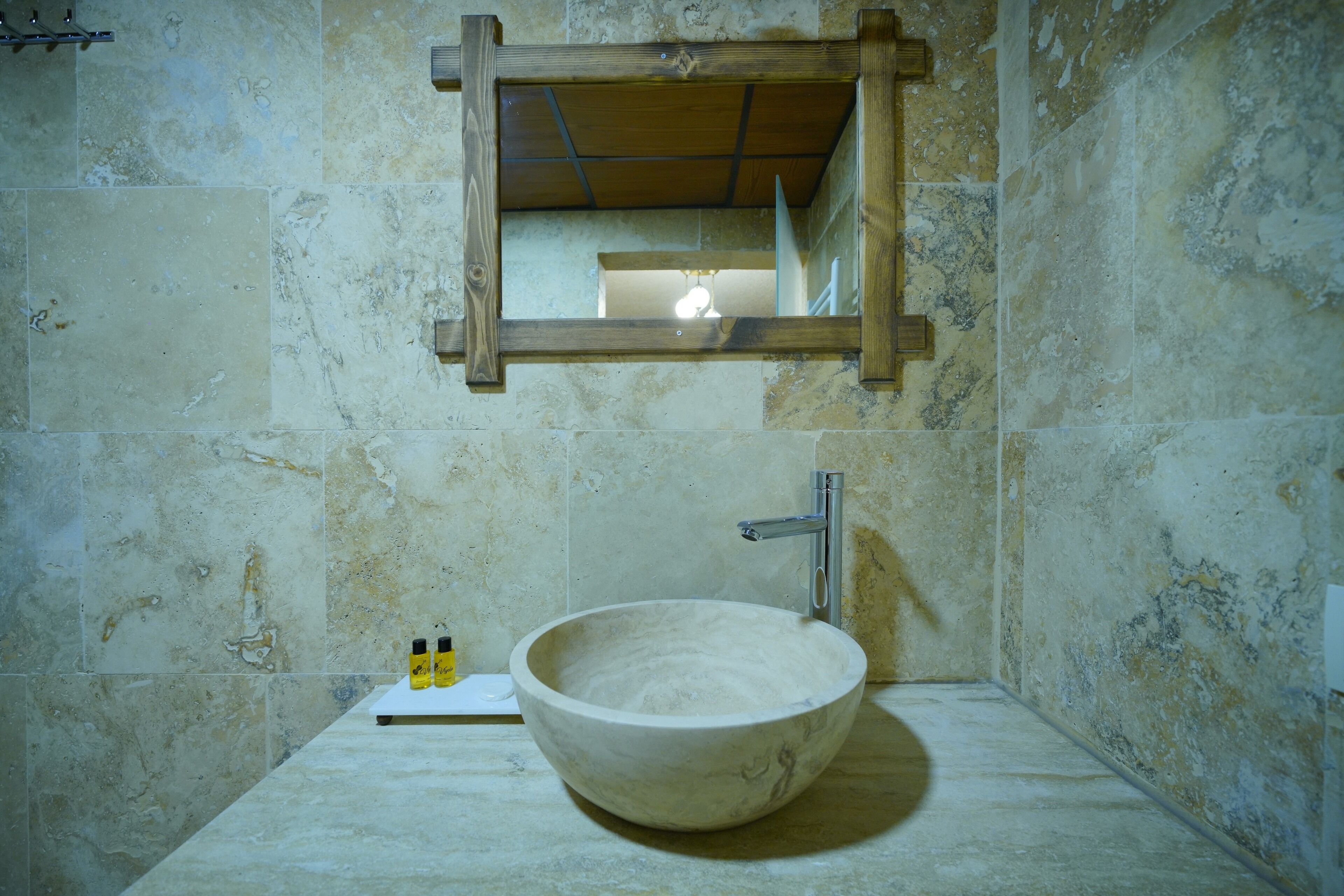 Un baño con un lavamanos grande, redondo y de cerámica blanca, un espejo con marco de madera y una única lámpara sobre el espejo.
