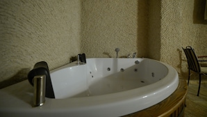 A bathtub in a room with textured walls and a wooden floor. - nirvana cave house hotel (Nevsehir)