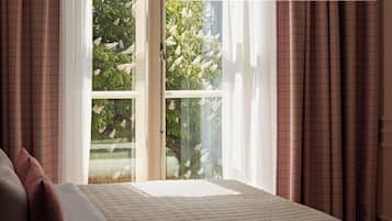 A bedroom with a bed, curtains, and a window with a view of trees and flowers.