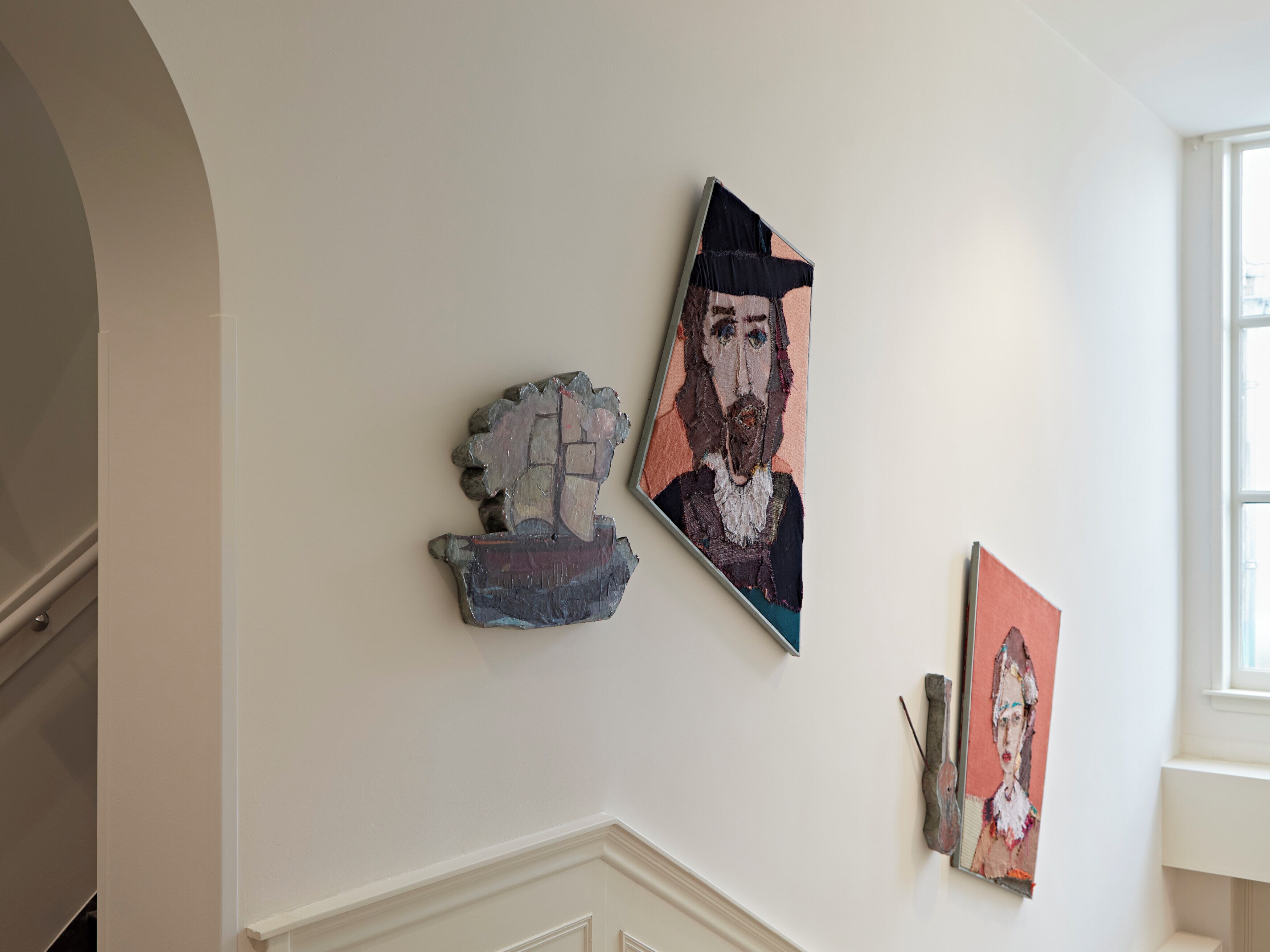 A hallway with three artworks on the wall, a staircase, and a window.