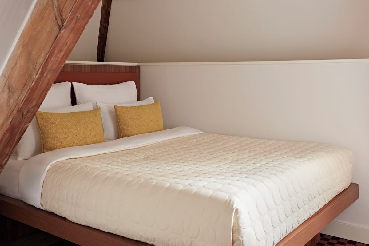 Een enkel bed met een houten hoofdbord, witte beddengoed en twee mosterdgele kussens.