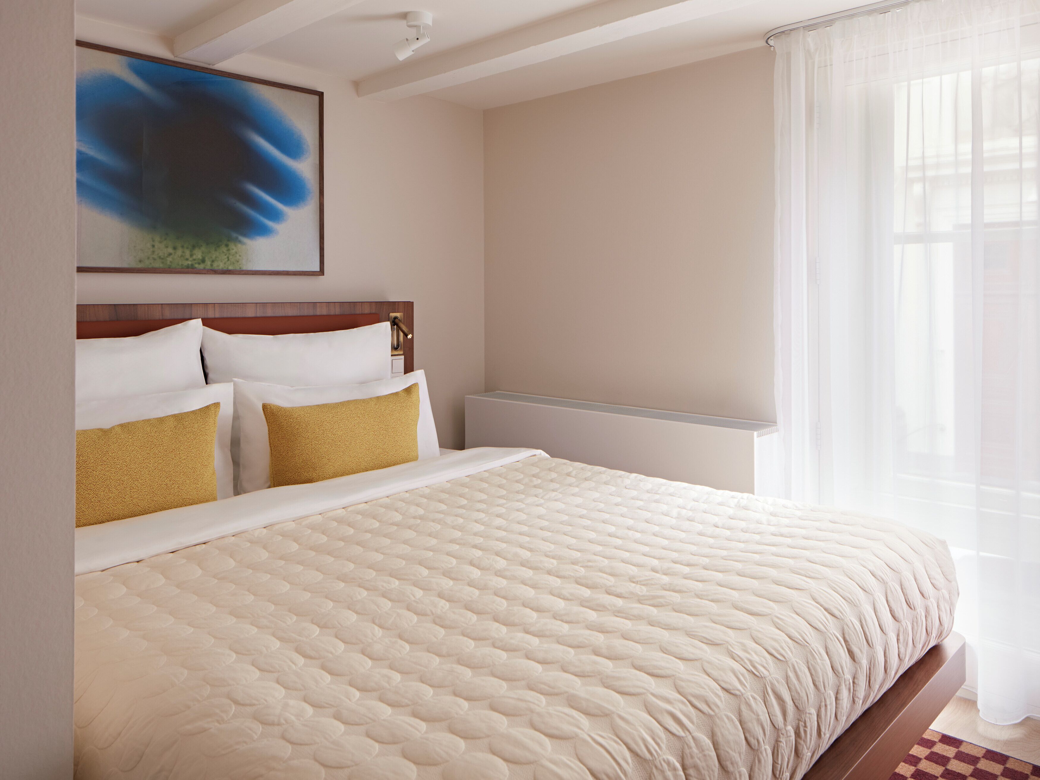 Habitación de hotel con una cama grande, cabecera, un cuadro en la pared y una ventana con cortinas.