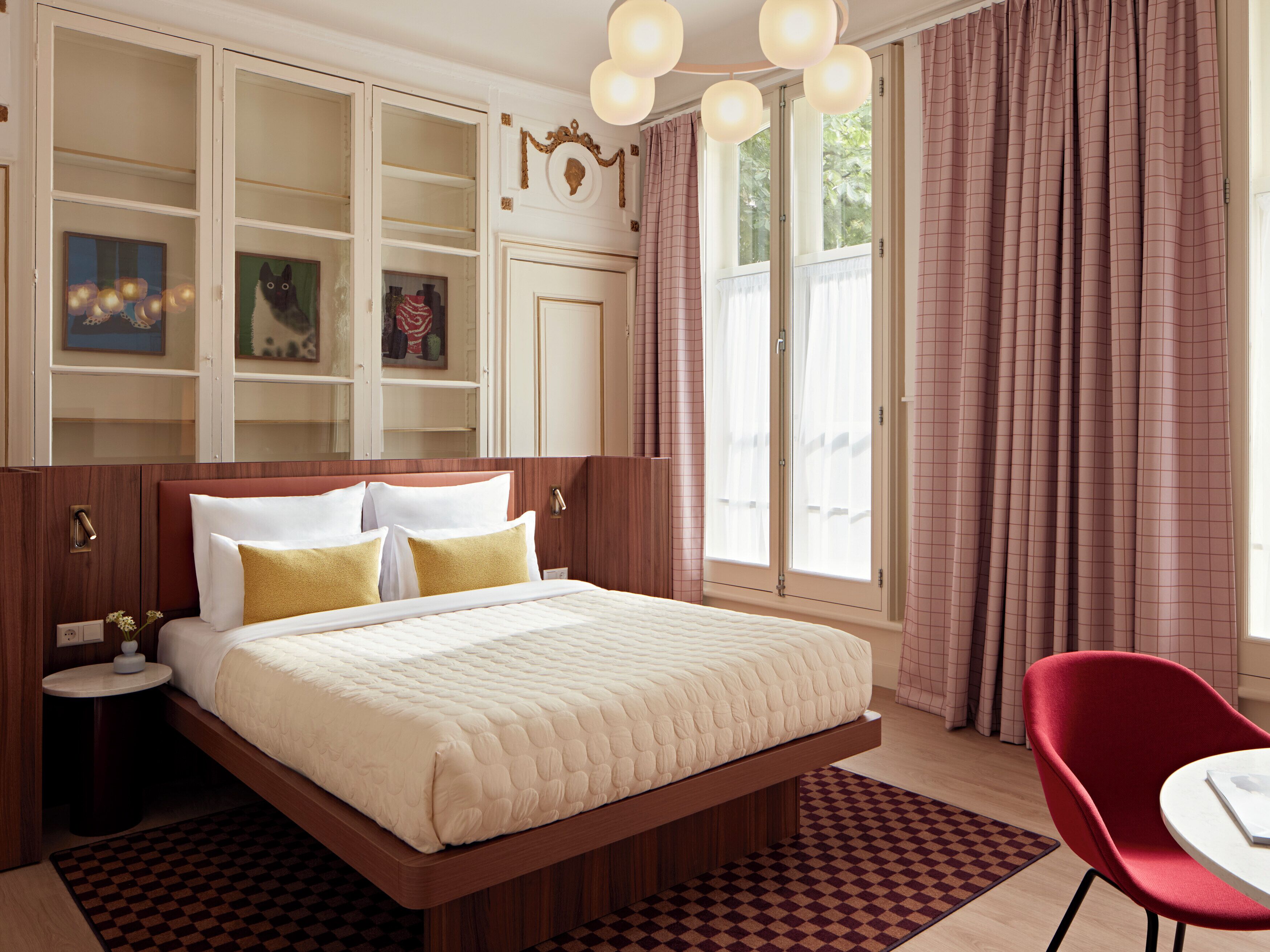 A bedroom with a bed, a nightstand, a chair, a window with curtains, and built-in shelving.