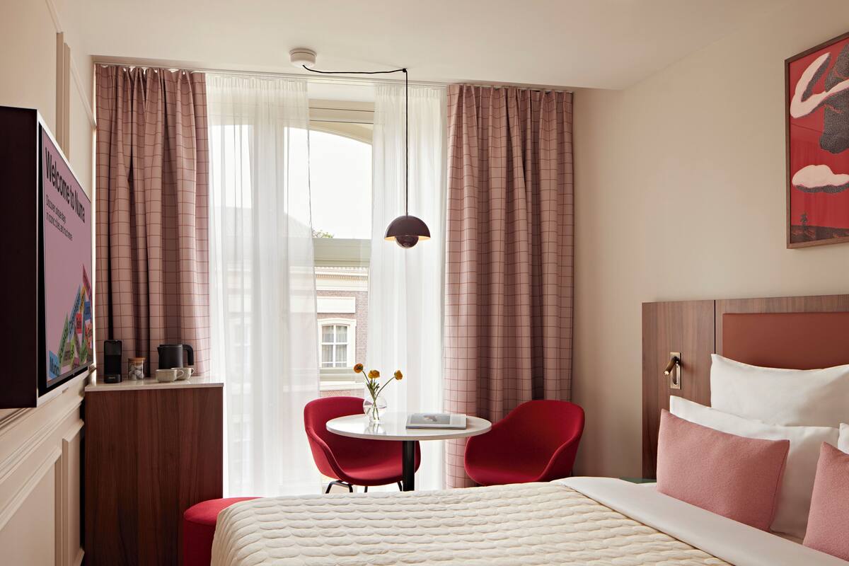 Een hotelkamer met een bed, een bureau met stoel, een kleine tafel met bloevas en een televisie aan de muur.