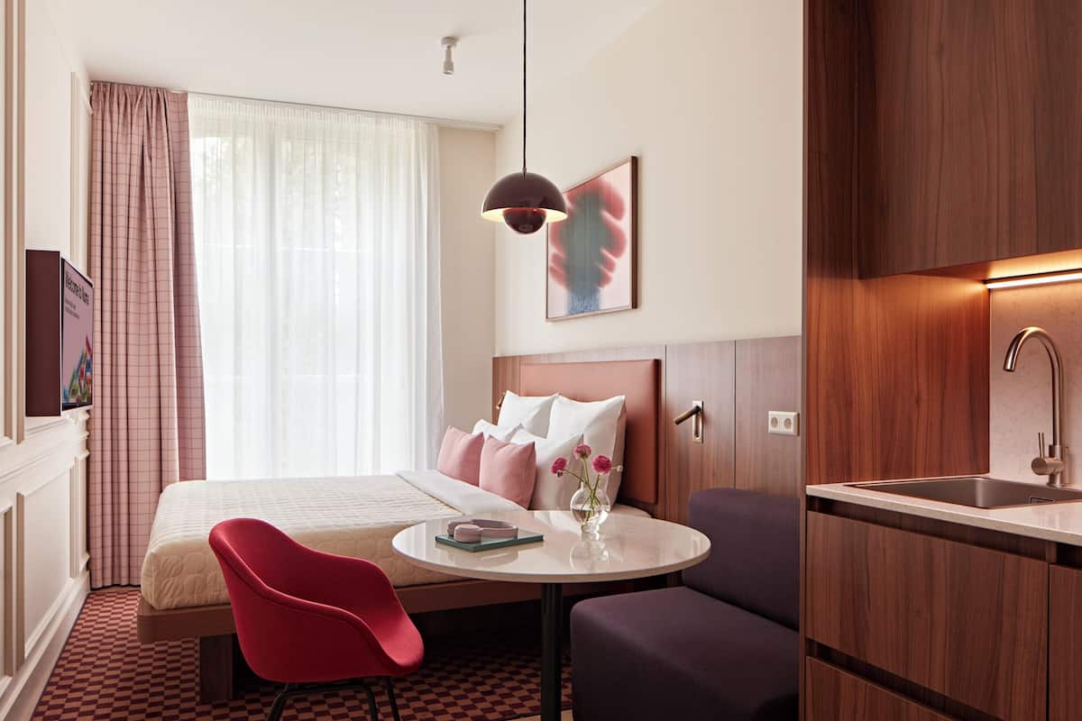 Een hotelkamer met een bed, een bureau met een stoel, een wastafel en een raam met gordijnen.