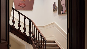 Een trap met houten spijlen, bekleed met een beige tapijt, en een muur met abstracte kunst.