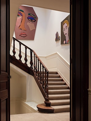 A staircase with wooden balusters, beige carpeted steps, and a wall with abstract art.