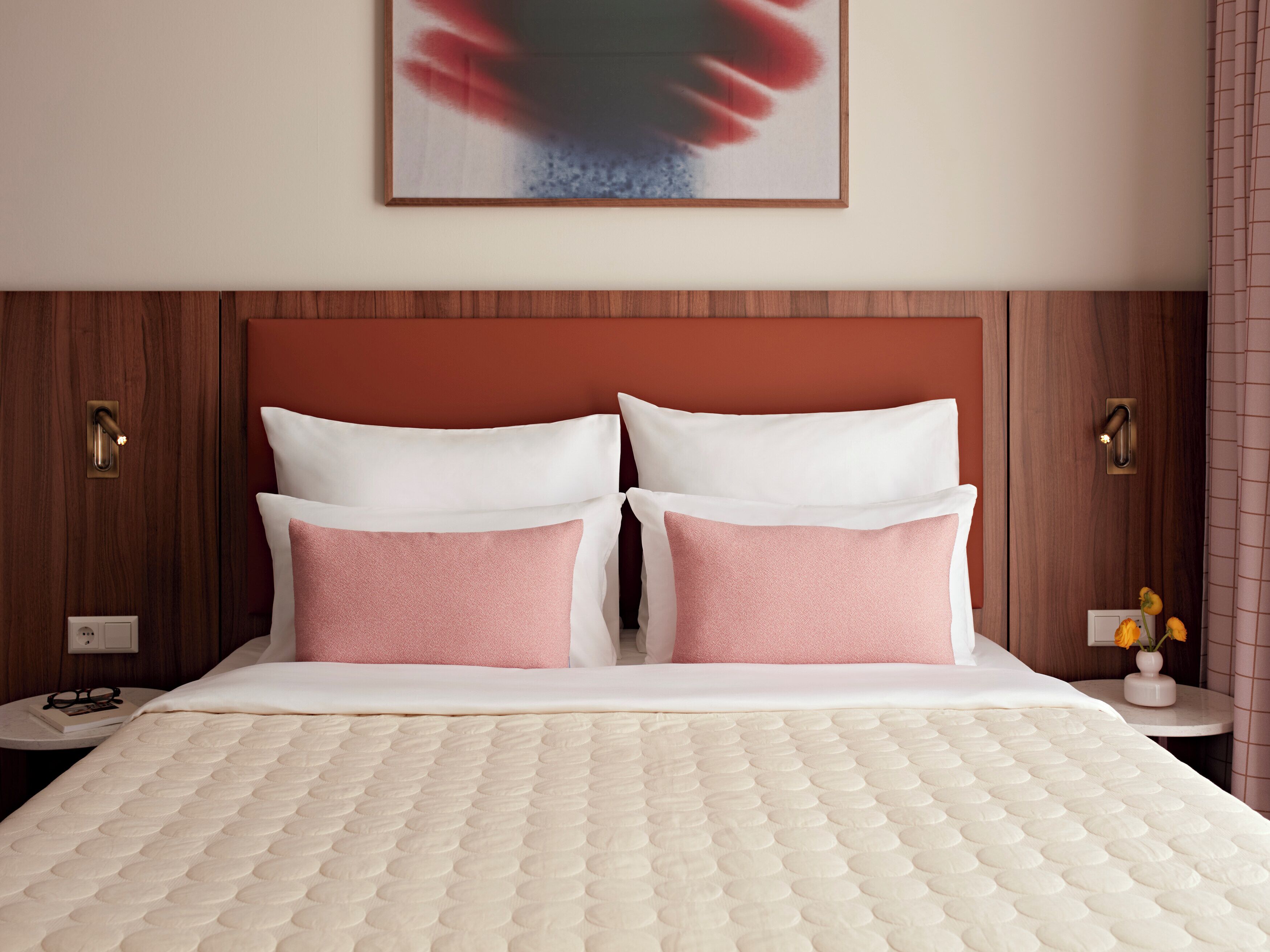 Een hotelkamer met een bed, twee nachtkastjes, een aan de muur hangend schilderij en een deur met een handvat.