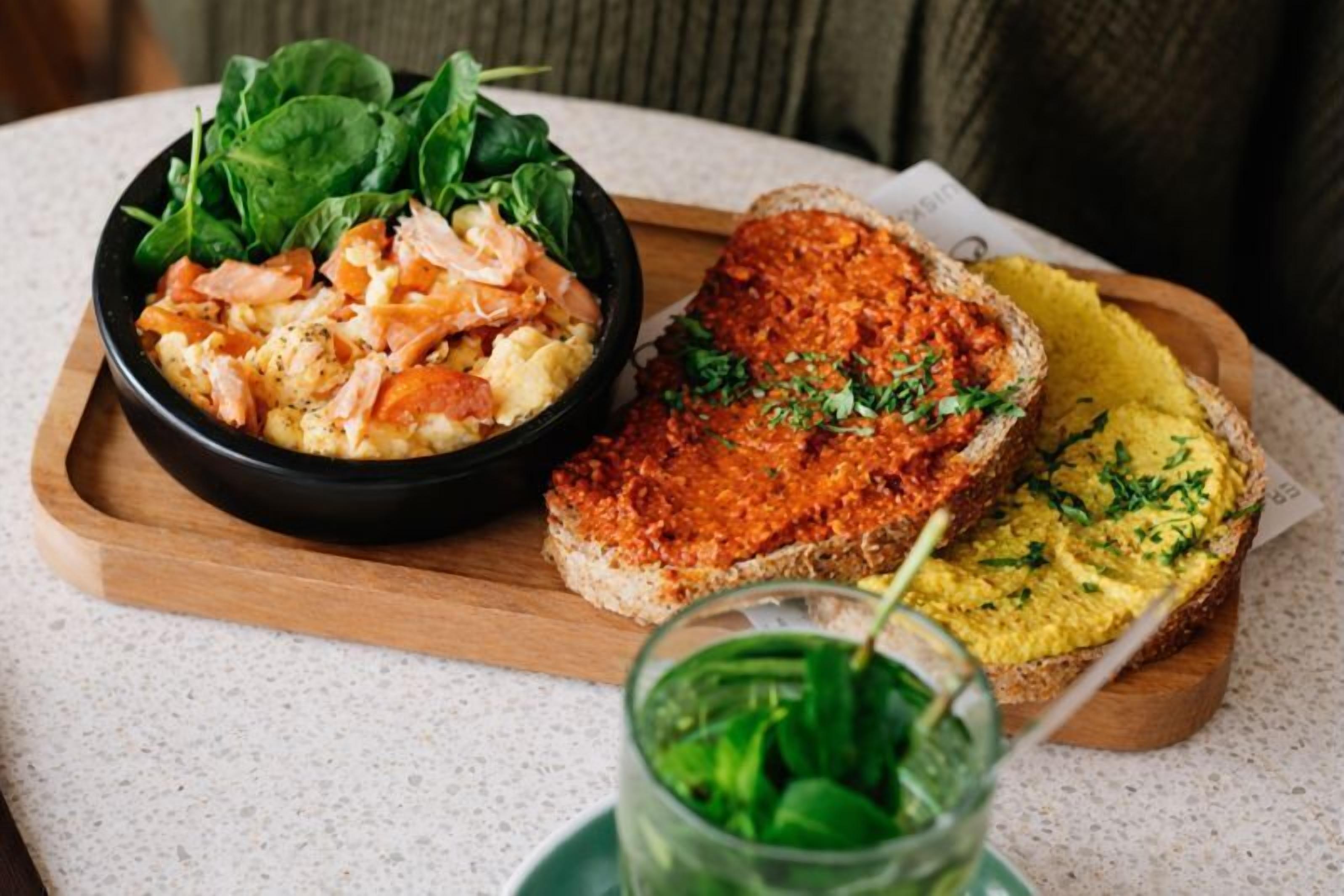 Un plato con salmón y huevos revueltos con espinacas, y dos tipos de pan con distintos aderezos.