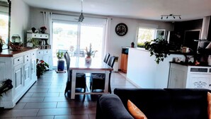 A spacious kitchen with a dining area, large windows, and a variety of plants.