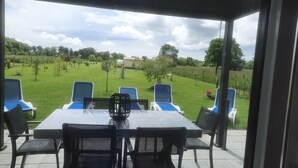 An outdoor patio with a table and chairs, overlooking a grassy area with trees and a fence.