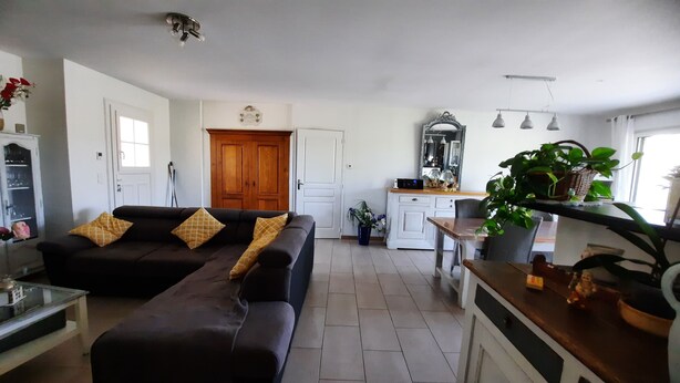 A living room with a sofa, a coffee table, and a dining area with a table and chairs. There is a kitchen area with cabinets and a microwave.