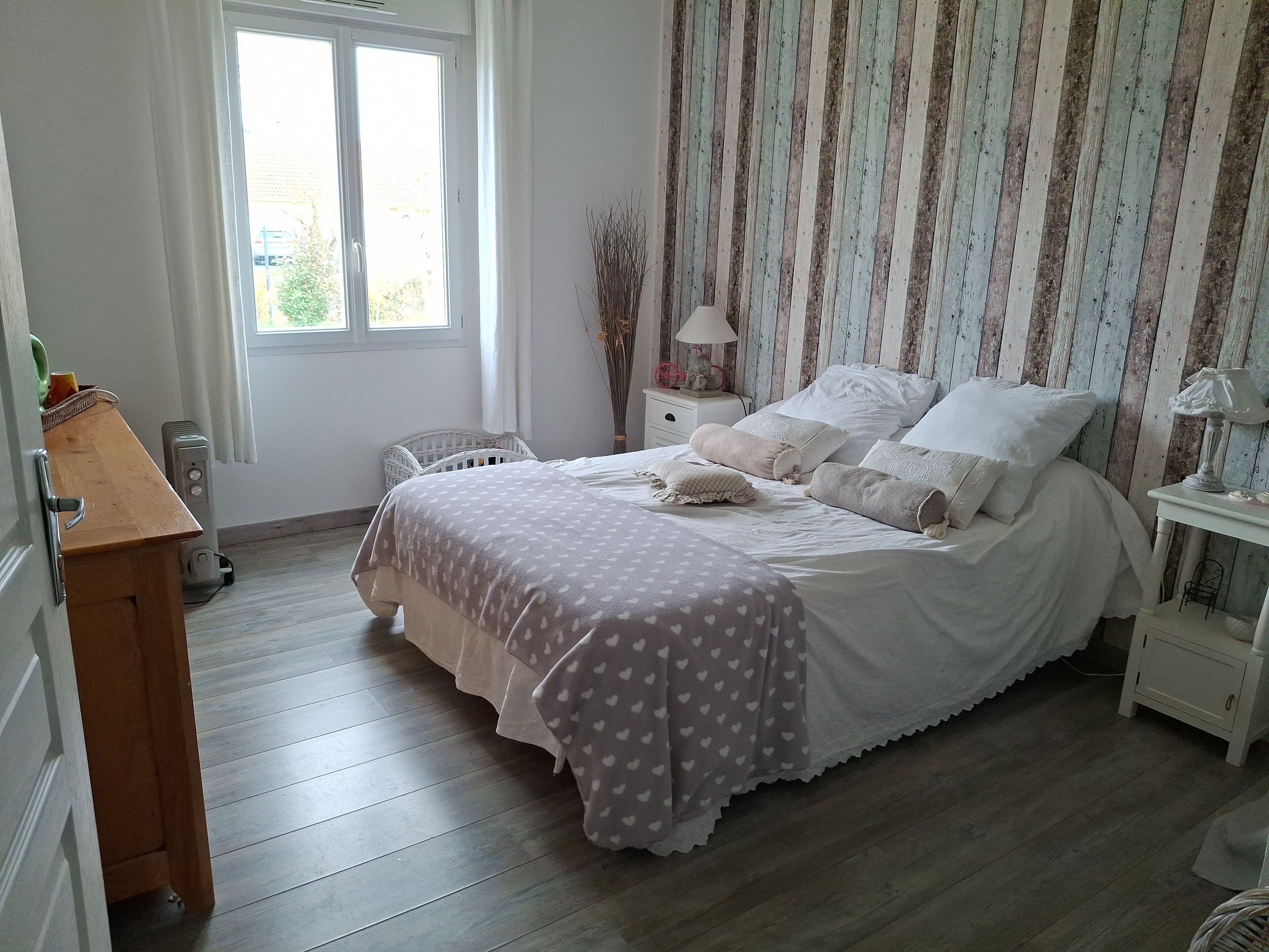 Une chambre à coucher avec un lit, des tables de chevet, une commode, une fenêtre et un plancher en bois.