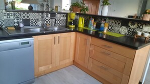 A kitchen with a dishwasher, wooden cabinets, a black countertop, and patterned backsplash.