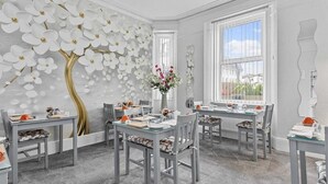 En matplats med modern design, med en vit och guldskimrande väggmålning, ett stort fönster med utsikt och ett bord dukat för fyra personer.