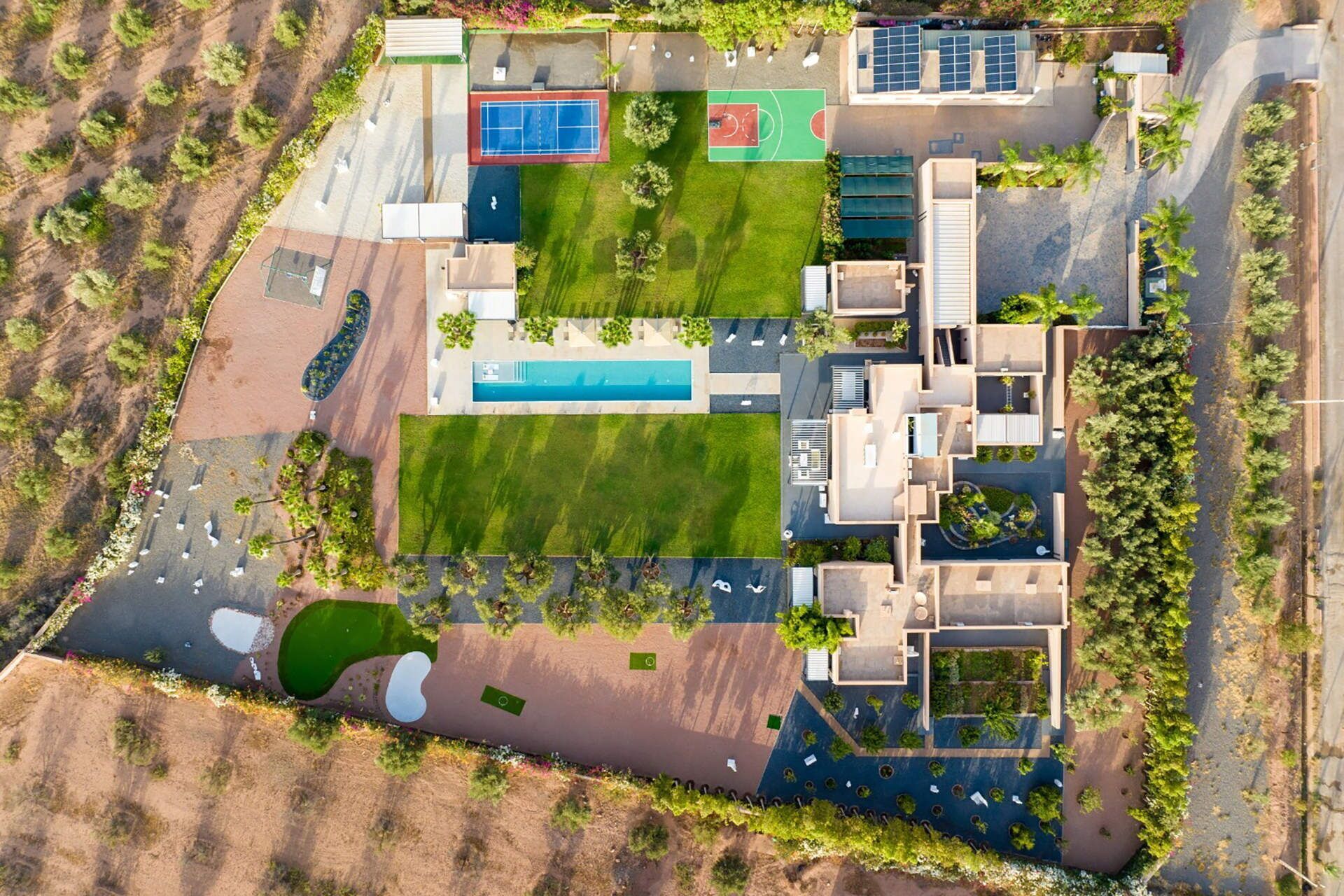 Vista aérea de un complejo residencial con varias edificaciones, piscina, canchas de tenis y un jardín ajardinado.