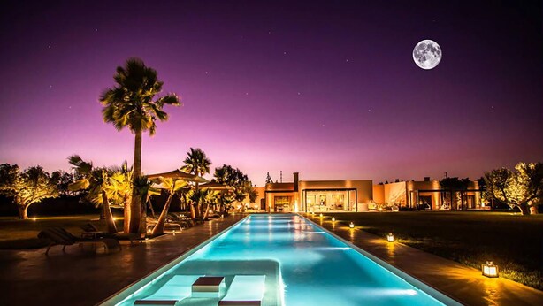 Ein Poolbereich bei Nacht mit Liegestühlen und einem Mond am Himmel.