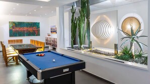 Ein moderner Poolbereich im Innenbereich mit Billardtisch, Sitzgelegenheiten und einem großen Fenster mit Kakteenausstellung.