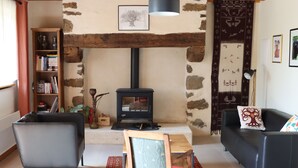 A cozy living room with a stone fireplace, a bookshelf, a sofa, and a table. - Renovated farmhouse in the heart of nature in the PNR de Millevaches en Limousin (Sussac)