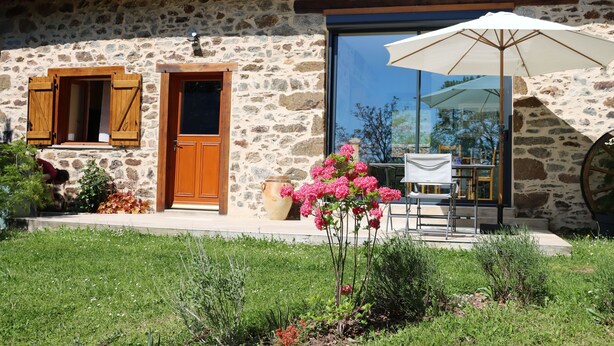 A stone house with a wooden door, large windows, and a patio with outdoor furniture. - Renovated farmhouse in the heart of nature in the PNR de Millevaches en Limousin (Sussac)