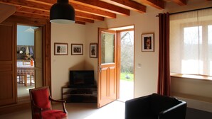 A room with wooden beams, a television, a red chair, and a large window with curtains. - Renovated farmhouse in the heart of nature in the PNR de Millevaches en Limousin (Sussac)
