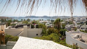 Un paisaje urbano costero con edificios, una masa de agua y colinas al fondo.
