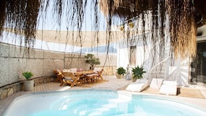 Una piscina con sillas de descanso y una mesa, rodeada de plantas en macetas y un muro de piedra.