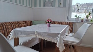 Uma área de refeições com mesa, cadeiras, um banco, uma janela com vista e um aviso na parede.
