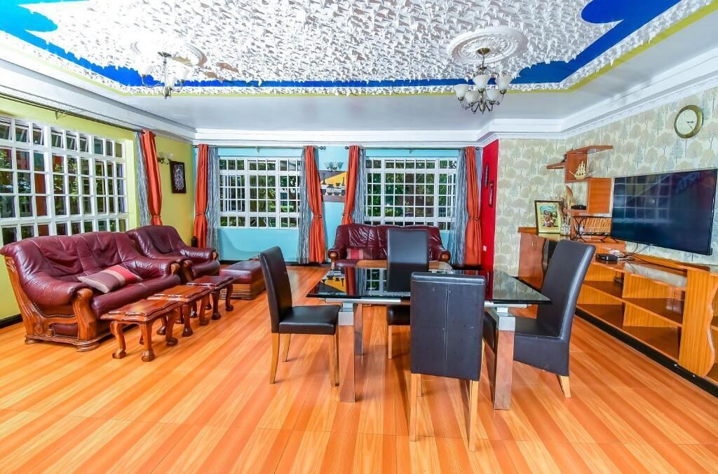 A spacious living room with a wooden floor, a red leather sofa, a glass coffee table, and a TV on a wooden stand.