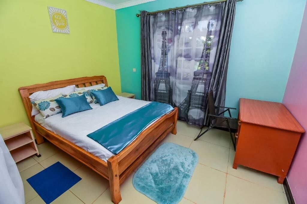 A bedroom with a wooden bed, a blue and white bedspread, a small desk, and a window with curtains.