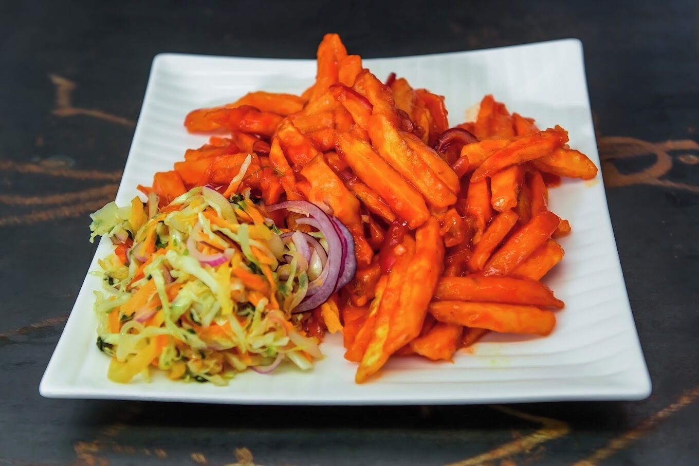 A white rectangular plate with a serving of sweet potato fries and a side salad.
