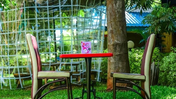 A small outdoor seating area with two chairs and a table, surrounded by greenery and a netted structure. - The Gems Resort Kutus (Kutus)
