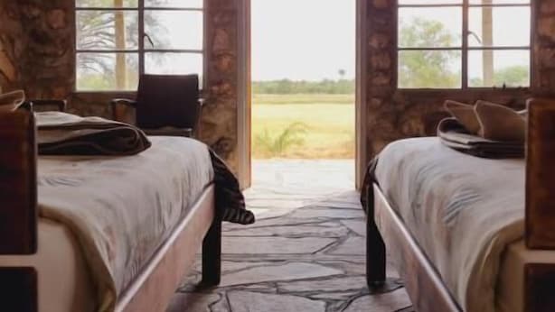 Une chambre rustique aménagée comme une tente, avec deux lits, des murs en pierre et de grandes fenêtres donnant sur le paysage extérieur.