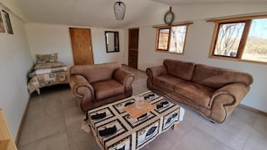 Un salon avec deux canapés marron, une table basse à motifs, une porte en bois et une fenêtre donnant sur un paysage agréable.
