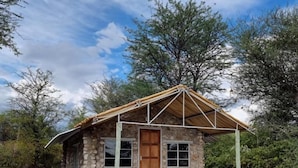 Un petit bâtiment en pierre, doté d’une porte et de fenêtres en bois, entouré d’arbres.