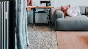 Una sala de estar acogedora con un sofá, una mesa con libros, una máquina de coser y un radiador.