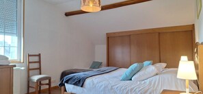 A bedroom with a wooden headboard, a bed with white linens and blue pillows, a chair, a bedside table with a lamp, and a window with blinds. - LE GITE DES DEUX LACS MORVAN NEAR LAC DES SETTONS 9PERS (Planchez)