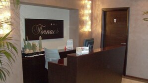 A reception desk with a sign that reads "Fornaci," a computer, and a chair. - Hotel Fornaci  (Trescore Balneario)