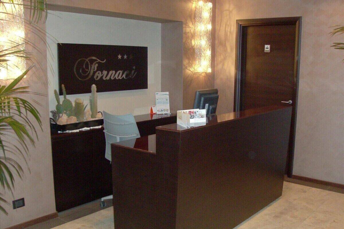 A reception desk with a sign that reads "Fornaci," a computer, and a chair.