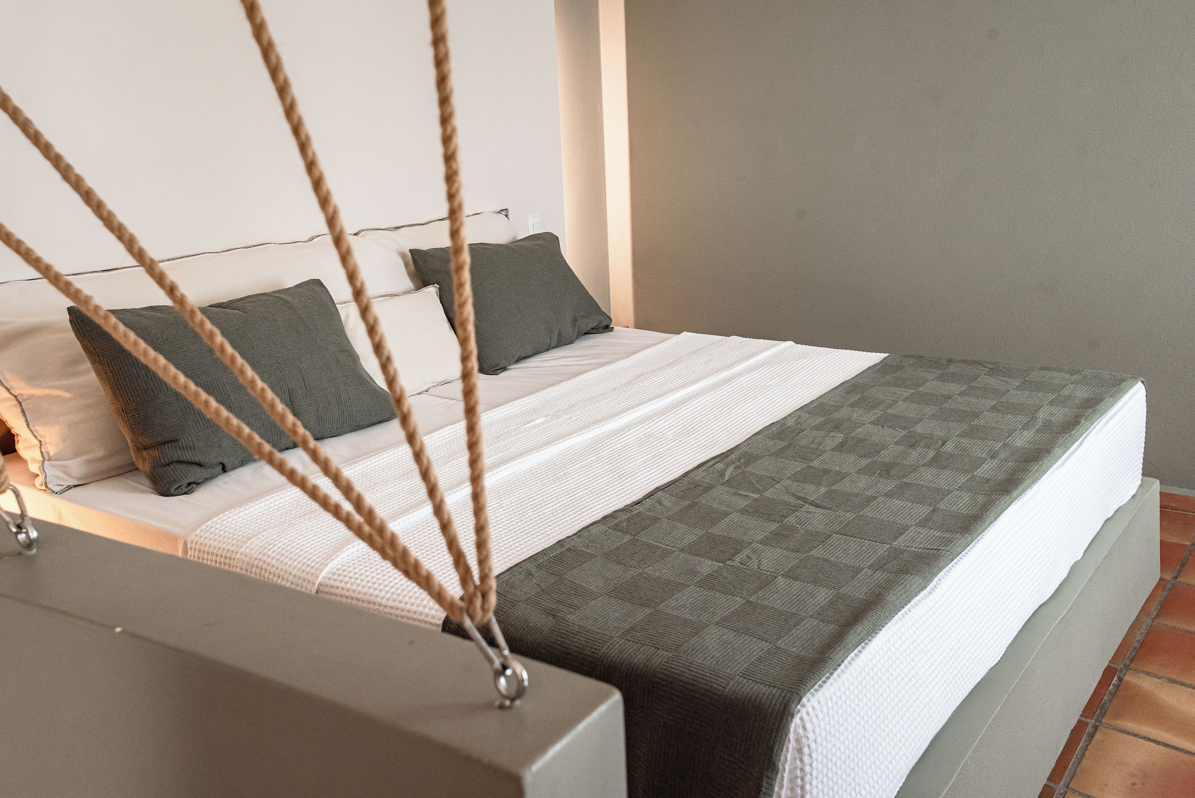Un lit avec un matelas blanc, des oreillers gris et une couverture matelassée grise.
