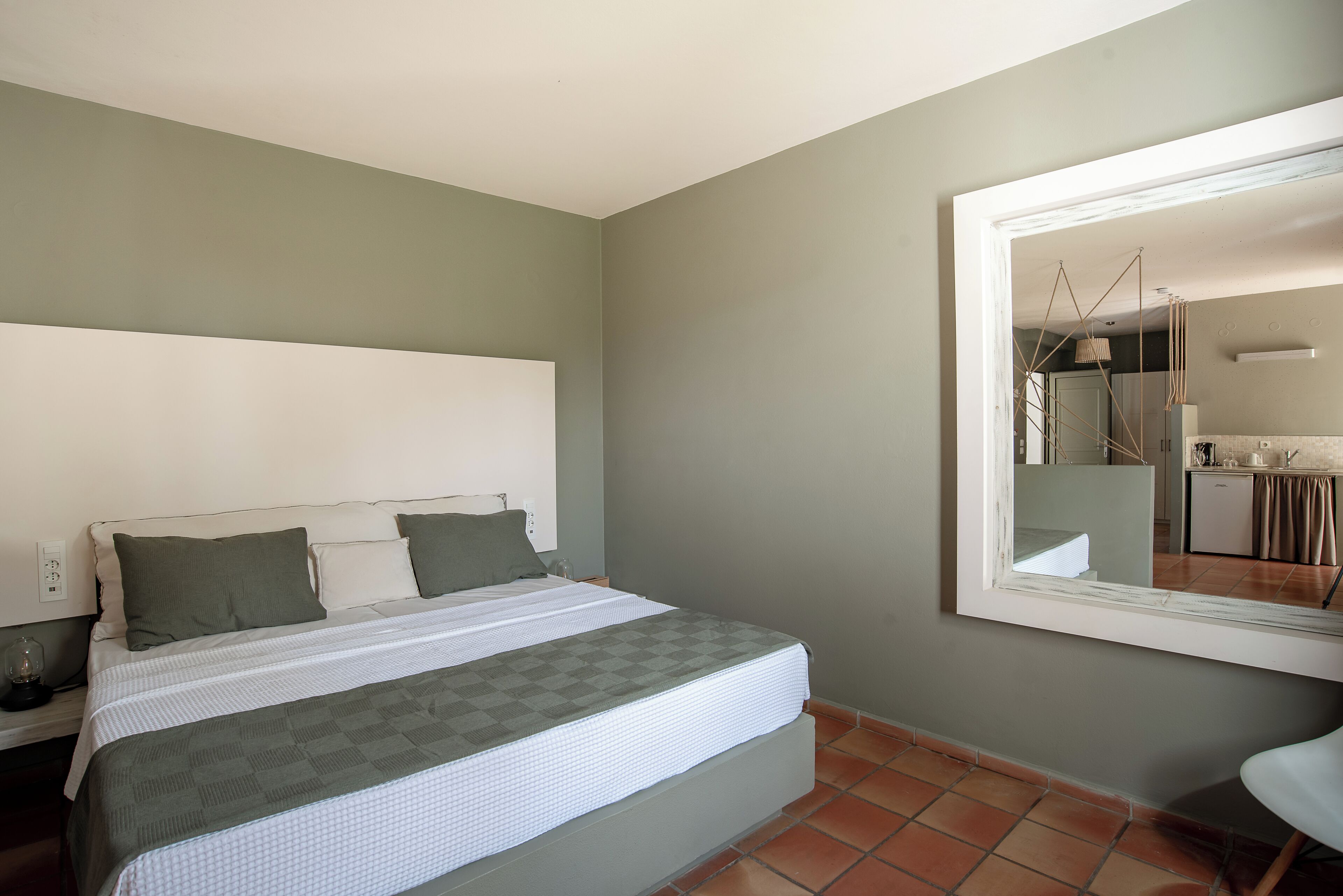 Un dormitorio con cama, mesita de noche, espejo y vistas a la cocina.