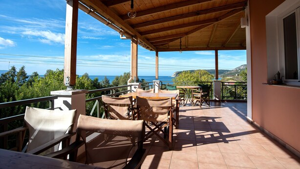 A covered outdoor seating area with a view of the sea, wooden furniture, and a tiled floor. - Mounda Beach Retreat (Skala)