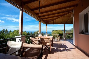A covered outdoor seating area with a view of the sea, wooden furniture, and a tiled floor. - Mounda Beach Retreat (Skala)